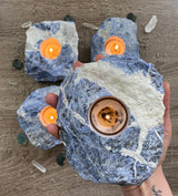 Illuminate your space with the enchanting beauty of Sodalite tea candle holders. These captivating gemstone creations, crafted from the mesmerizing blue hues of Sodalite, infuse your surroundings with a serene and tranquil ambiance. Embrace the metaphysical properties of Sodalite as it promotes peace, harmony, and enhanced communication. 